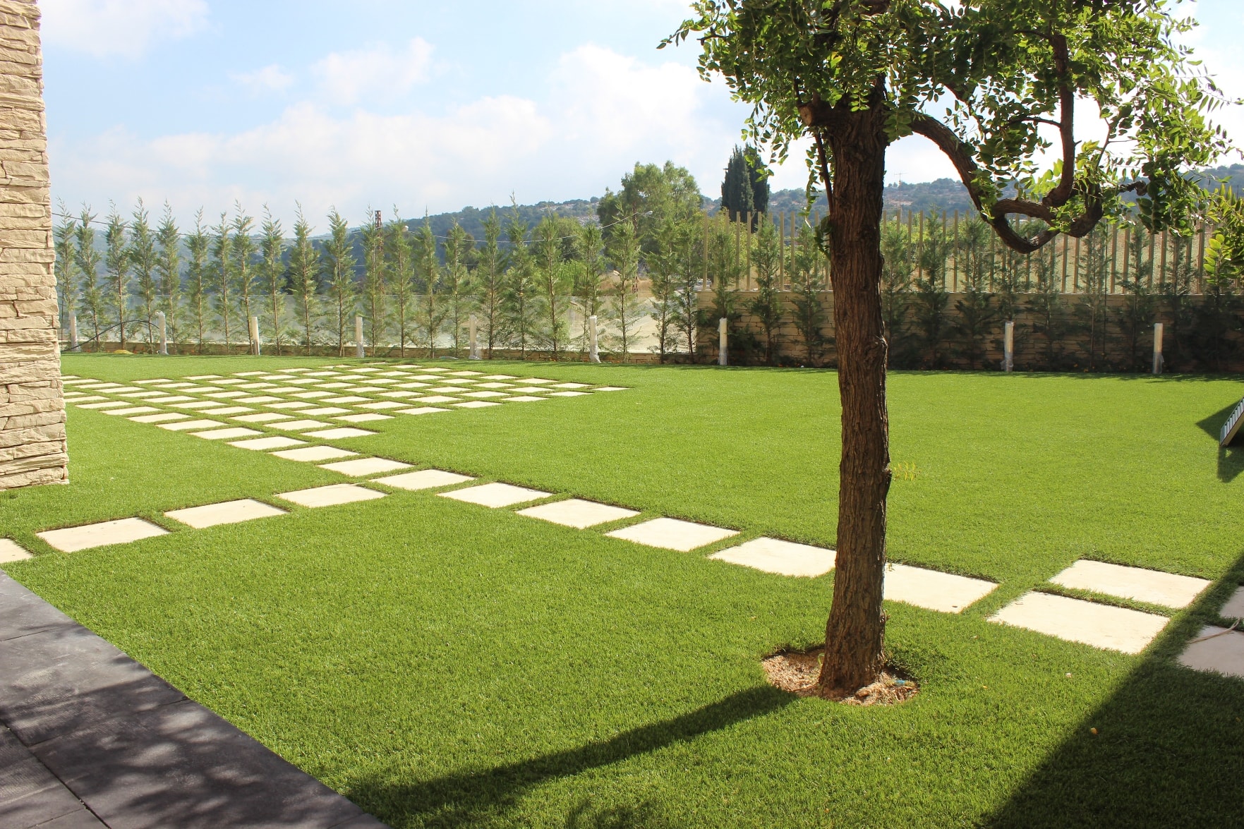 Artificial turf installation by Southwest Greens featuring a lush, low-maintenance synthetic lawn with modern stone paver walkway and landscaped backyard design.